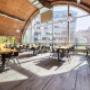 Offener Sitzbereich mit großen Panoramafenstern und gemütlichem Holzboden in den Brandauer Bierbögen. Wiener Wirtshauskultur trifft auf modernes Loft-Design und entspanntes Ambiente.