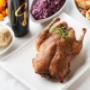 Knusprig gebratene Ente mit Serviettenknödeln, Rotkraut und fruchtiger Sauce auf weißem Teller, dazu Rotwein – herzhafte österreichische Wirtshausküche im Silberwirt in Wien.