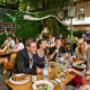 Belebter Gastgarten des Wirtshauses Silberwirt in Wien-Margareten mit Holzbänken, Gästen beim Essen und Trinken und schattigen Bäumen – gemütliches österreichisches Restaurant mit Garten.