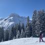 Skifahrer und Kind auf Skipiste mit verschneiten Bergen und Bäumen und blauem Himmel Skifahrer und Kind auf Skipiste mit verschneiten Bergen und Bäumen und blauem Himmel