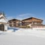 Außenansicht Familienhotel Sonnenburg  im Winter mit blauem Himmel und im Vordergrund die Kapelle der Sonnenburg inmitten der Skipiste