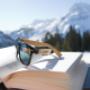 Sonnenbrille auf Buch auf Balkon am Zimmer und verschneite Berge in Oberlech