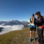 Wanderer auf Bergwiese über Nebeldecke mit Berggipfeln und blauem Himmel