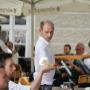 Service im Gastgarten beim Stift Heiligenkreuz: Kellner serviert Speisen unter Sonnenschirmen, im Hintergrund spielt eine Kapelle – gemütliches Kloster bei Wien und Ausflugsziele Niederösterreich.