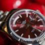 Detailaufnahme des roten Zifferblatts mit feiner Linienstruktur und Wochentagsanzeige. Die Balance zwischen Eleganz und Ausdrucksstärke macht diese Rolex zu einem echten Highlight.