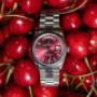Die Rolex Day-Date mit rotem Zifferblatt im Fokus – eingebettet in pralle Kirschen. Das Bild wirkt frisch, leidenschaftlich und außergewöhnlich – eine Uhr, die Blicke fesselt.