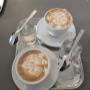 Zwei frisch zubereitete Cappuccinos mit cremigem Milchschaum - serviert mit einem Glas Wasser, perfekt für eine genussvolle Kaffeepause