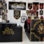 Ein Blick auf den Empfangsbereich des Studios Happy Needles Tattoo. Hinter dem schwarzen Tresen mit goldener Beschriftung hängen dekorative Wandteppiche, Kunstwerke und das markante Studio-Logo in Schwarz-Gold. Auffällig ist die Mischung aus sakralen, mys