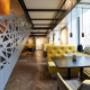 Im Koinonia+ Restaurant Wien erwartet die Gäste ein heller Gastraum mit eleganten Holztischen und langen gelben Sitzbänken. Die großen Fenster bringen viel Tageslicht ins Lokal und sorgen für ein freundliches Ambiente – perfekt für gesellige Runden, Busin