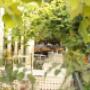 Blick durch grünes Blattwerk auf den gemütlichen Gastgarten des Ponykarussells im Wiener Prater – helle Tische, viel Natur und entspannte Atmosphäre für Frühstück, Kaffee und kleine Pausen im Grünen.